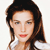 Pixelated portrait of a person with long brown hair, light skin, and red lips wearing a white top against a plain background.