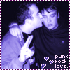 Two people in a dark setting with purple-tinted lighting; one person kisses the other's cheek while making a peace sign, text reads 'punk rock love.'