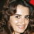 Pixelated close-up of a person with dark curly hair, light skin, and a red accessory on the right side, smiling with visible teeth.