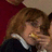 A pixelated image shows a person with light brown hair holding an object near their mouth, set against dark green and gray backgrounds with red text.