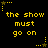 Yellow pixelated text "the show must go on" on black background with yellow star and dotted line decorations.