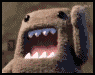 Animated brown plush creature with large black eyes and white teeth, mouth open in a wide grin