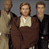 Static 49x49 pixel icon showing three figures in brown and beige clothing against a gray background, with visible dithering and low-resolution rendering artifacts.