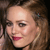 Pixelated close-up of a person with light brown hair, red lips, and a small hair accessory, set against a dark background.