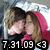 Two people in a close embrace with one wearing a pink hooded garment, set against a blurred background with visible date text at the bottom.