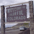 A pixelated sign with partially legible text reading "HILL" and "BROOK" in a dark frame, mounted on a pole with a blurred background.
