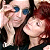 Two people in close physical proximity, one with light skin and blue eyes wearing a dark top, the other with red hair and fair skin also in dark clothing.