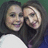 Two people with dark hair pose closely together, smiling at the camera against a green background.