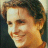 Pixelated close-up of a person's face with light brown hair, smiling expression, and warm-toned skin under soft lighting.