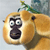 A pixelated cartoon monkey face with wide eyes and a dark nose, set against a light background with a green stem-like shape above.