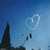 Pixelated blue sky background with a white heart-shaped trail and dark silhouettes of buildings or structures.