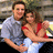 A pixelated static image shows a man and woman embracing, the man in gray shirt and dark pants, the woman in red top and white skirt.