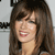 A pixelated close-up of a person with long brown hair and bangs, smiling with visible teeth and red lips against a light background.