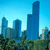 Pixelated cityscape with blue skyscrapers against a light blue sky, green foliage at the bottom, and no visible text or motion.