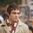Pixelated static image of a person with short brown hair wearing a white and red striped shirt against a blurred background.