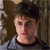 Static pixelated image of a person with short dark hair wearing a light gray shirt over a dark collar, set against a blurred brown background.
