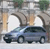 A static pixelated image shows a dark blue sedan with four visible wheels parked under a concrete archway, with light-colored pillars and greenery in the background.