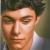 Pixelated close-up of a person's face with light skin tone, dark hair, and closed eyes against blurred background.