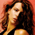 A pixelated close-up of a person with long brown hair wearing a black top against a reddish background.