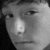 Grayscale pixelated image of a person's face with visible eyes, nose, and mouth, showing partial facial features and a bright reflection on the nose.