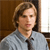 Pixelated portrait of a person with light brown hair wearing a light blue collared shirt and dark tie against a brown wooden background.