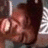 Pixelated close-up of a person's face with dark hair, light skin, and a blurred background featuring vertical light and dark stripes.