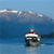 A small boat with a white hull and dark cabin floats on blue water under a light blue sky with scattered clouds.