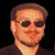 Static pixelated image of a person's face with sunglasses against dark background, rendered in low-resolution style typical of early internet icons.