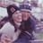 Two people in a close embrace, one wearing a dark cap with a light-colored logo, both in light and dark clothing, with a blurred background.
