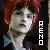 Pixelated portrait of a person with red hair and light skin, wearing dark clothing against a dark background.