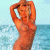 Pixelated image of a person in an orange swimsuit standing by water with arms raised above head, light blue background.