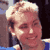 Pixelated static image of a person with light-colored hair and visible facial features in close-up, set against dark background elements.