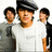 Three pixelated figures stand side-by-side against a white background; the central figure wears a black cap and white shirt, flanked by two others in dark and light clothing.