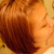 A person with reddish-brown hair in a side profile view, showing subtle facial features and warm-toned background.