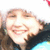 Pixelated close-up of a smiling person with light brown hair and dark clothing against a bright background.