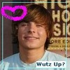 A person with light brown hair wearing a light blue shirt, with a pink heart-shaped graphic overlay and text reading "Wutz Up?" at the bottom.