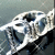 Pixelated static image of a white and dark-colored object with curved shapes against a muted gray background.