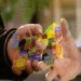 Pixelated static image of hands holding a colorful object with blurred background.