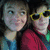 Two people in a close-up pose, one wearing yellow sunglasses and red clothing against a light background.