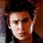 Pixelated close-up of a person with dark hair against warm brown background, wearing black clothing and white earpieces.