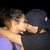 A pixelated static image shows a person with light skin and brown hair in an embrace, wearing dark clothing against a black background.
