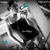 A pixelated grayscale image with a central black shape resembling an abstract form, surrounded by light and dark gray tones, featuring two small cyan accents.
