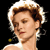 Pixelated close-up of a person with light brown hair styled in an updo, wearing a white strapless garment against a black background.