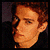 Pixelated image of a person with reddish hair and dark clothing against a dark background, showing slight facial expression variation.