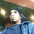 A person in a blue hoodie and dark beanie appears in four with slight variations in head position against a green textured background with circular lights