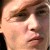 Pixelated close-up of a person's face showing eyes, nose, mouth, and light brown hair against a blurred background.