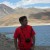 Pixelated figure in red shirt stands against blurred beach background with water and sky.