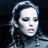 A pixelated image of a person with light-colored hair styled in an updo, wearing dark clothing against a black background.