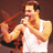 Pixelated image of a man with light brown hair and beard wearing a white tank top, holding a red object near his face against a dark brown background.