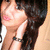A pixelated close-up of a person with long dark hair, light skin, and pink lips wearing a white top with thin straps.
